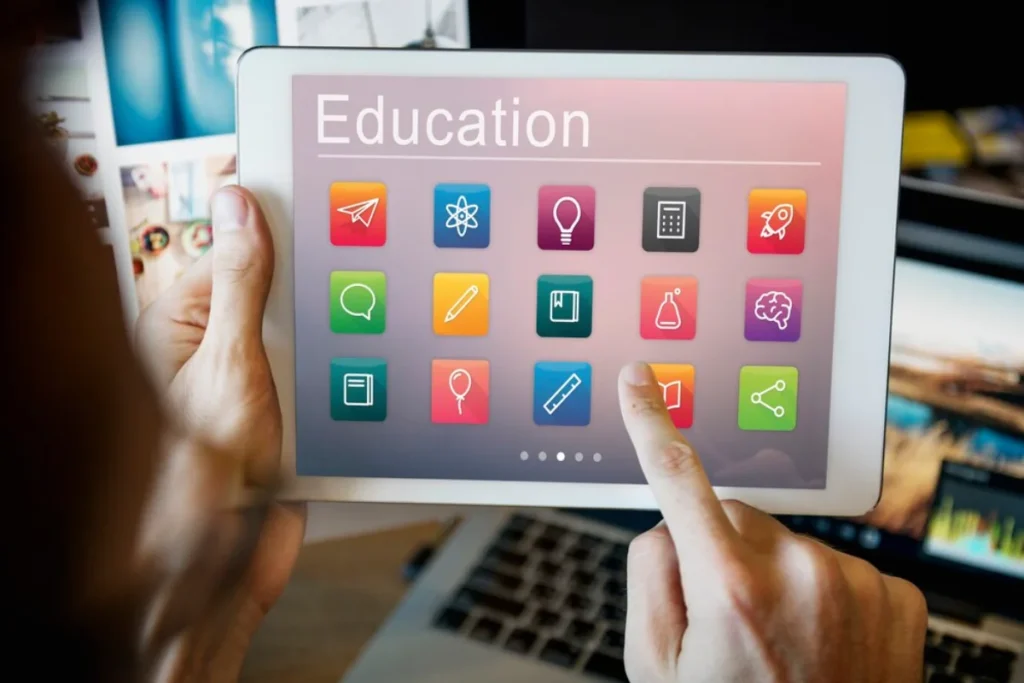A person holding a tablet displaying a colourful screen with icons labelled with education-related symbols