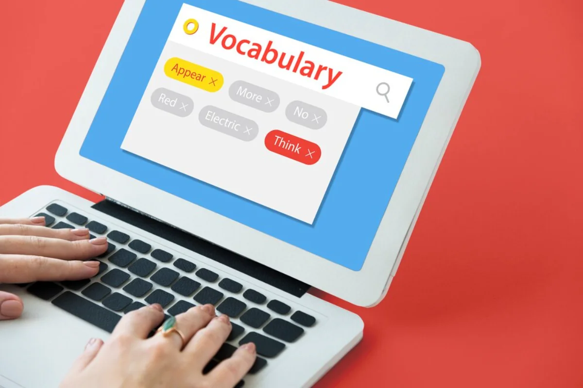 Hands typing on a laptop keyboard with a digital vocabulary learning application displayed on the screen, showing various words with options to select or remove them.